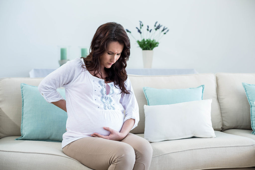 woman having a lower back pain from her pregnancy while sitting on the sofa